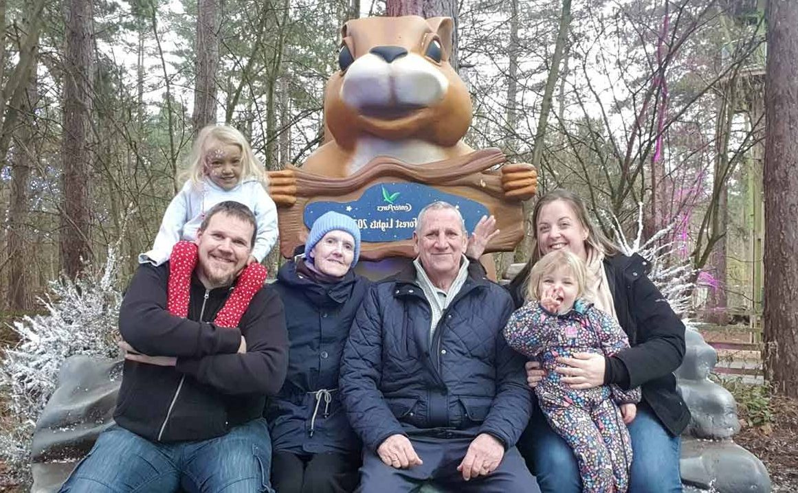 A family of 6 smile for a photo together in front of a sculpture of a squirrel