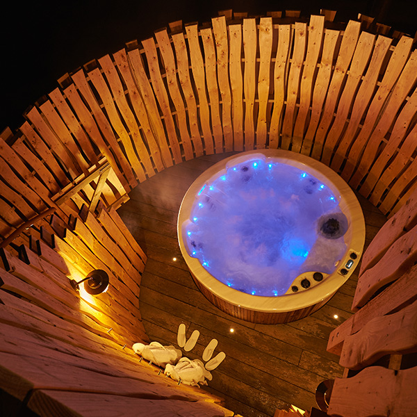 A view down a spiral staircase to a private outdoor hot tub lit up at night. 