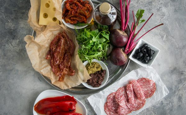 The ingredients needed for the muffaletta laid out including salami, bacon, cheese and peppers
