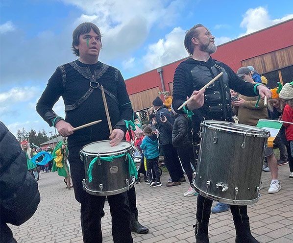 Two people carrying and playing drums in a parade