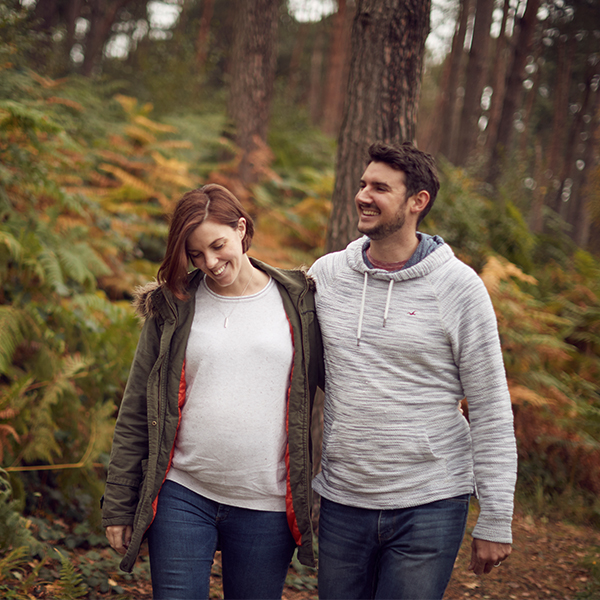 Expecting parents stroll through woods