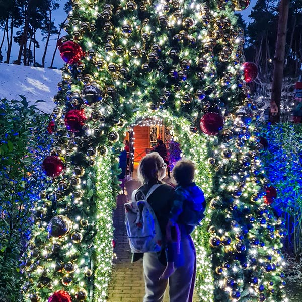 mum holding little one walking under a lit Christmas tree arch