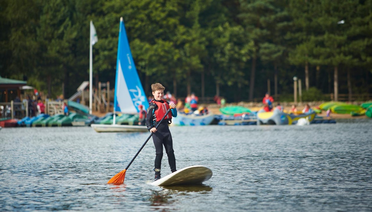 A boy balances on a stand up paddleboard at the lake.