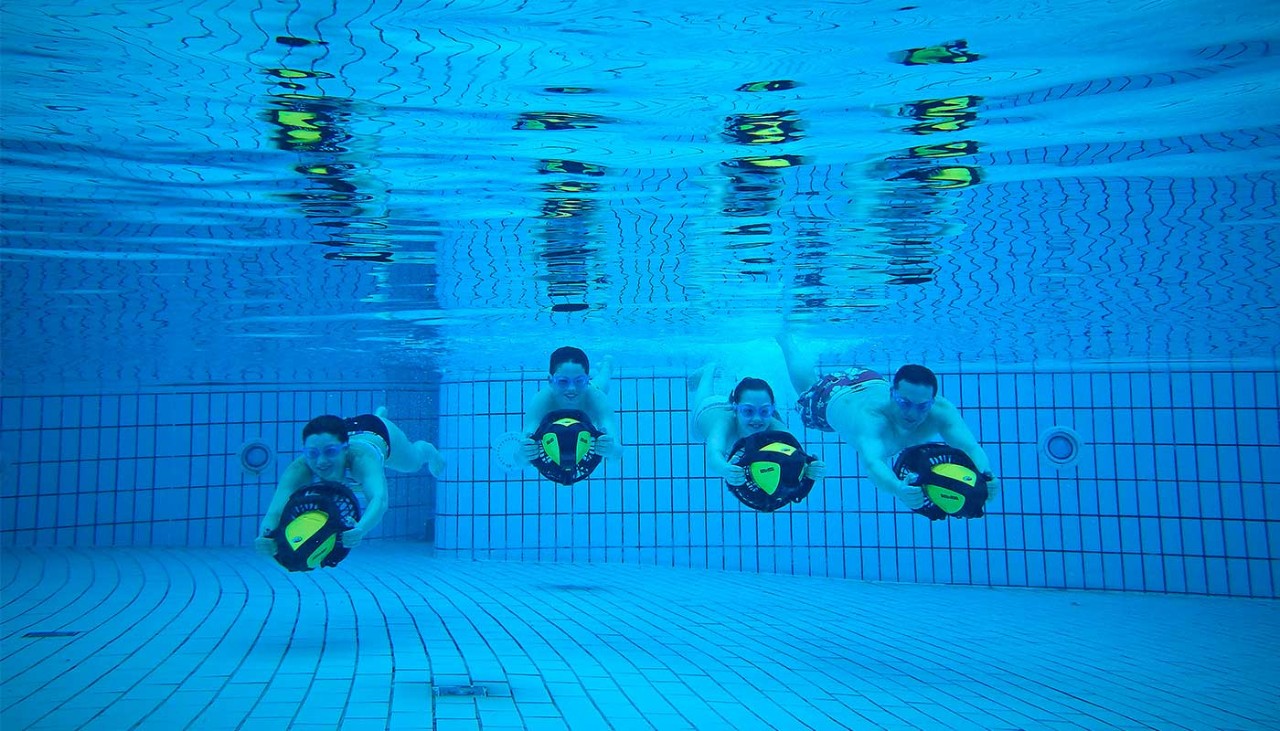 One male adult and three children swimming with aqua-jets in the pool.