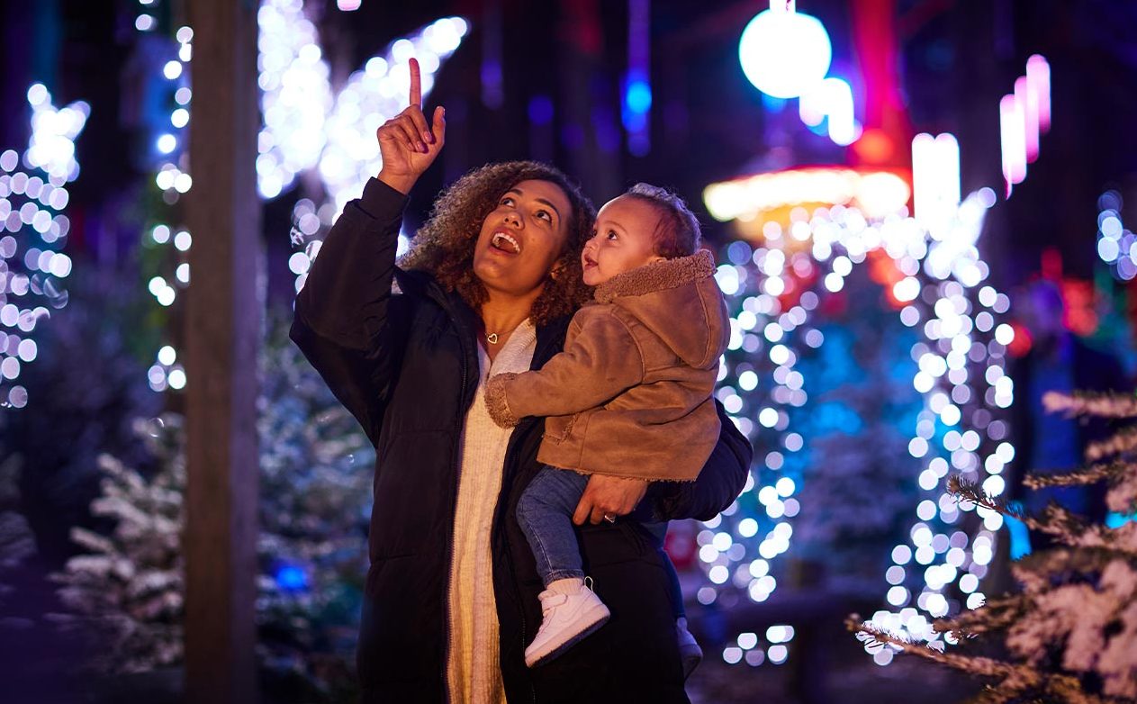 Mum holding baby in arms and whilst pointing up at the twinkling lights