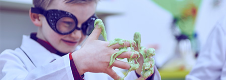 A child wearing a lab coat and goggles playing with slime.