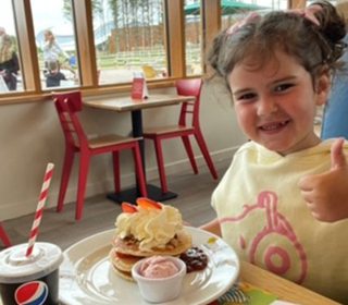 young-girl-with-her-thumbs-up-and-smiling-with-a-plate-of-pancakes-and-cream