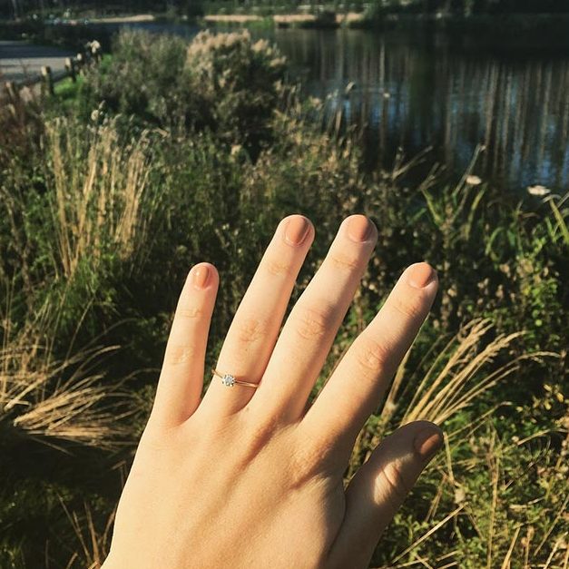 Aimee's hand with an engagement ring on her finger, with the lake in the background