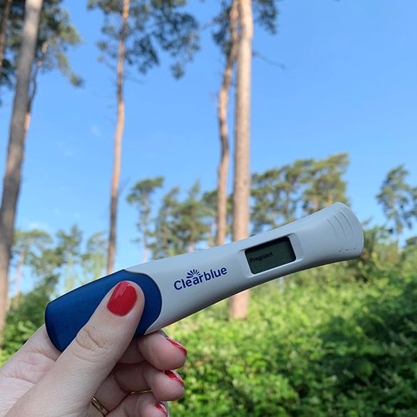 Image of a positive pregnancy test being help amongst the trees