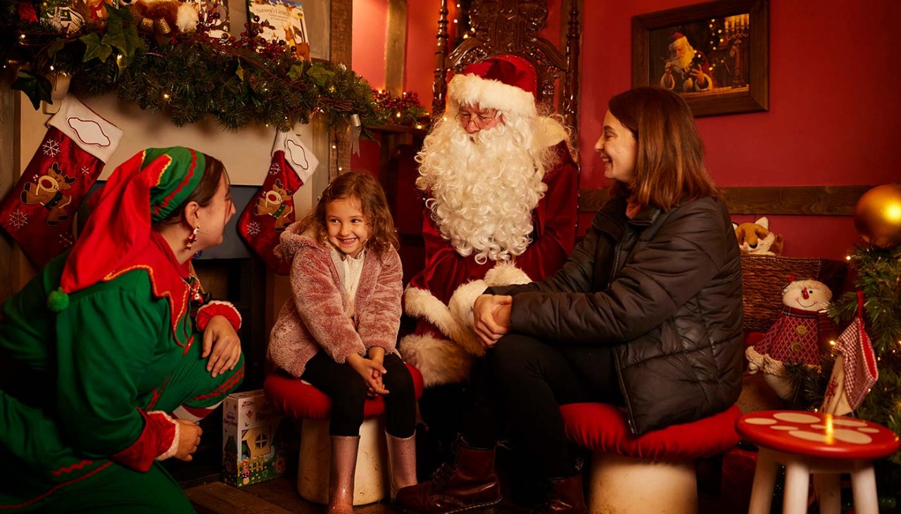 A little girl smiles as she meets Santa and one of his elves