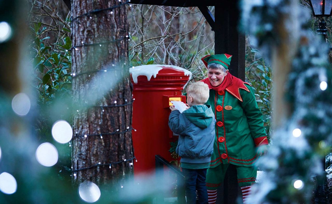 little boy with elf posting his letter in Santa's postbox