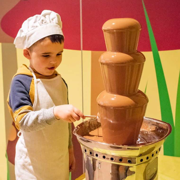 A little boy covering his marshmallow in chocolate using a chocolate fountain