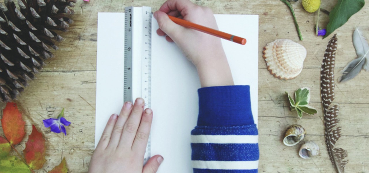 Hands using a ruler to draw lines on a paper, surrounded  by natural trinkets like a feather and a pinecone.