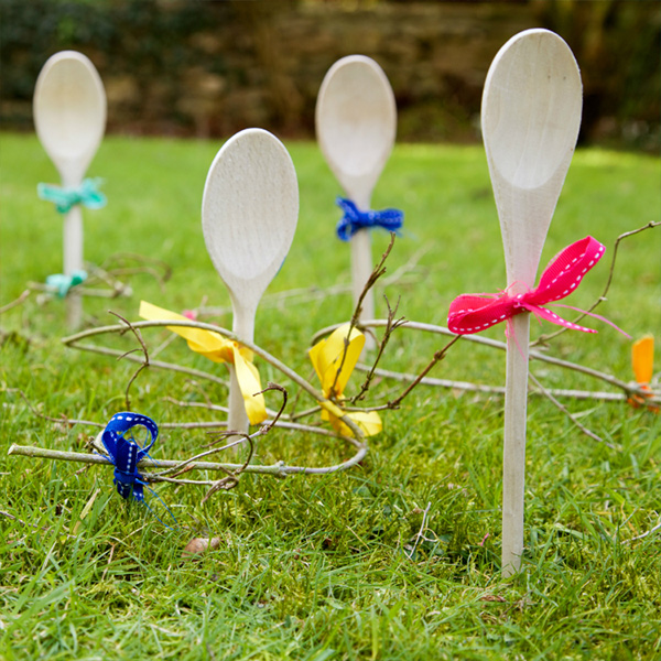 Wooden spoons decorated with ribbons, stuck in the ground to be used for a ring toss. 