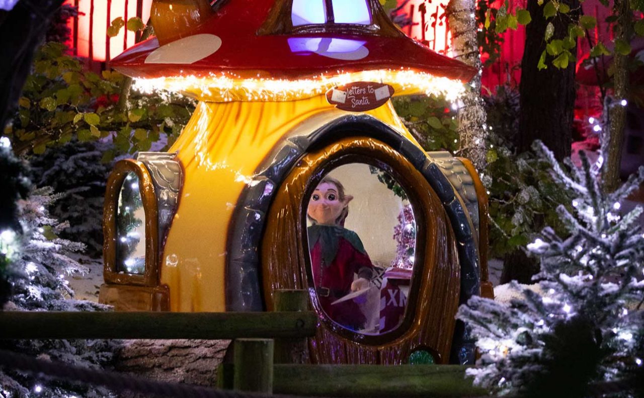 Toadstool lit up with animatronic elf inside surrounded by snowy trees