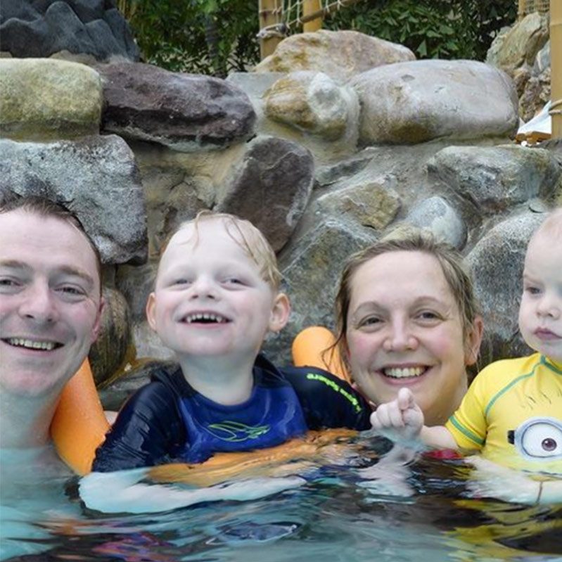 Two children and their parents smile together in the outdoor pool