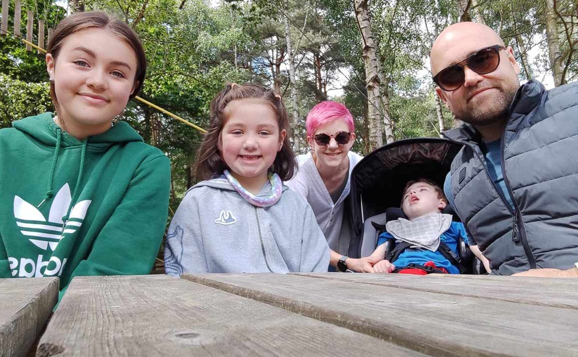 A family of 5 sitting at a picnic bench smile for a photo