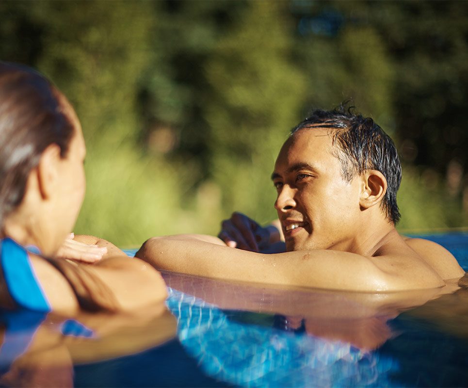 A couple in an outdoor pool overlooking the forest, looking at each other