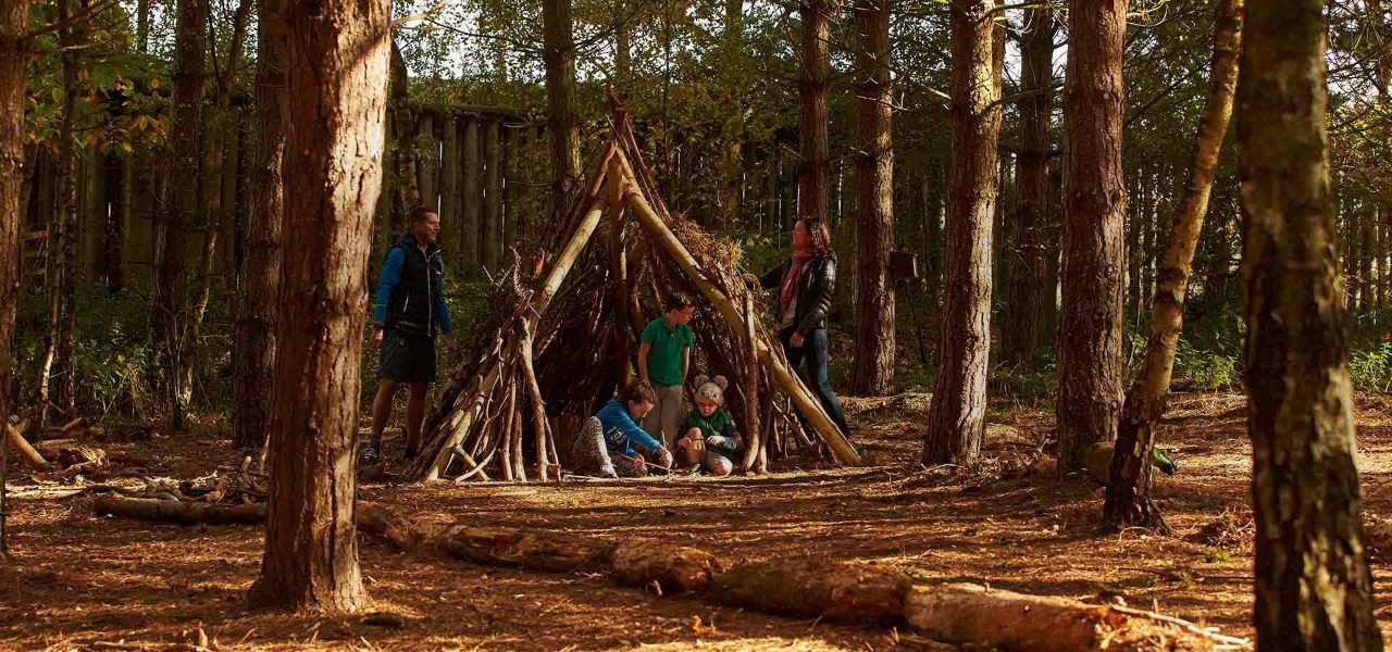 A family in a pyramid shaped den made of logs.