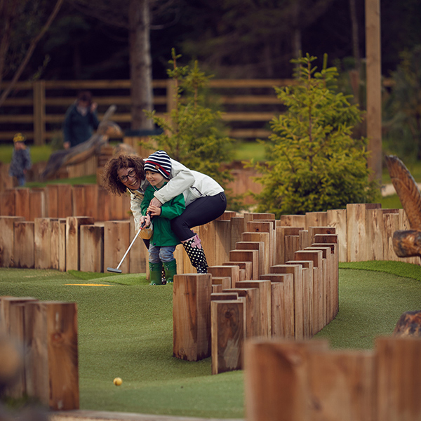 A mother helping her child use a golf club on a mini golf course.