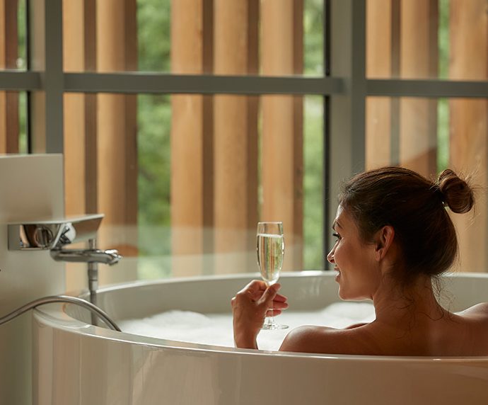 A woman enjoying a bath overlooking the forest with a glass of prosecco.