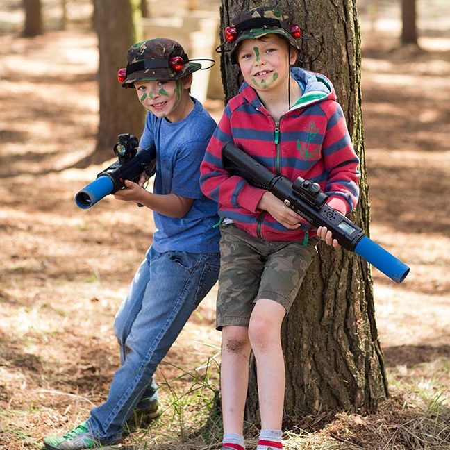 Two children hide behind a tree whilst enjoying Laser Combat