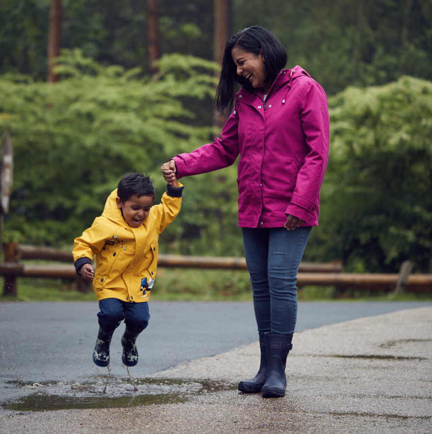 Child jumps in puddle whilst walking with mother