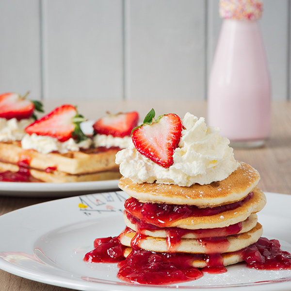 A stack of pancakes layered with strawberry jam and whipped cream.