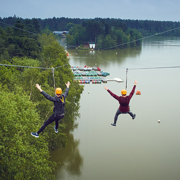 Two people ziplining over the lake.