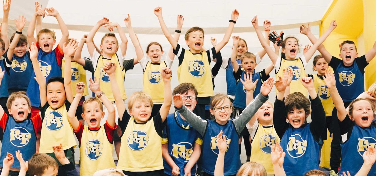 A group of children wearing sports bibs cheering 