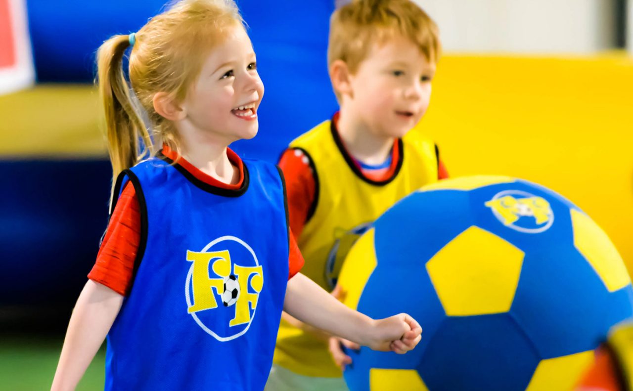 A little girl and boy playing with a giant soft football 