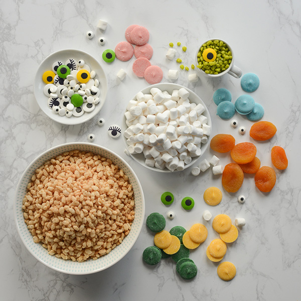 Ingredients laid out on a table including crispy cereal, icing eyes, marshmallows and colourful chocolate.