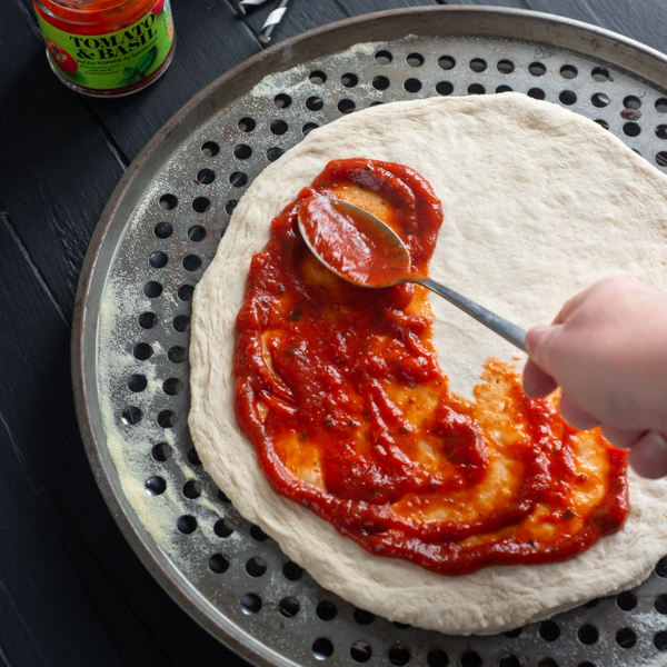 Tomato sauce being spread across pizza base