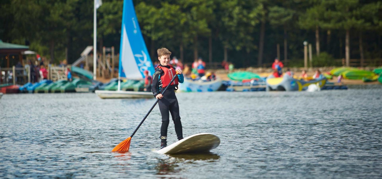 A boy smiles as he balances on a paddleboard on the lake
