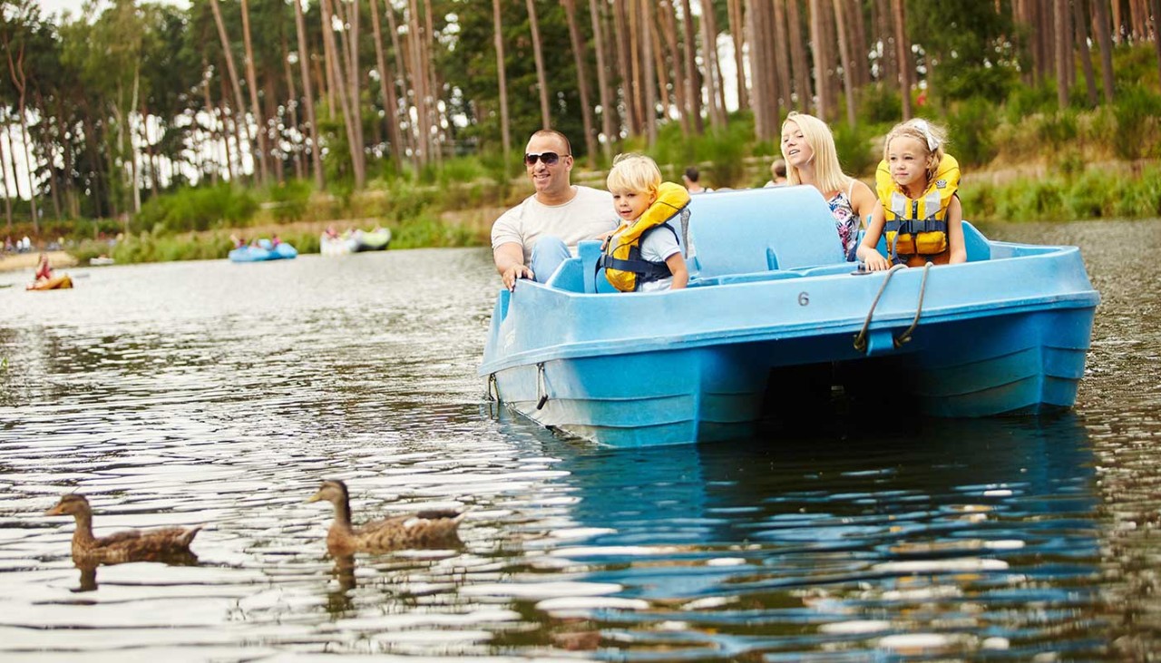 A family take a ride on a pedalo and smile as they look at the ducks on the lake