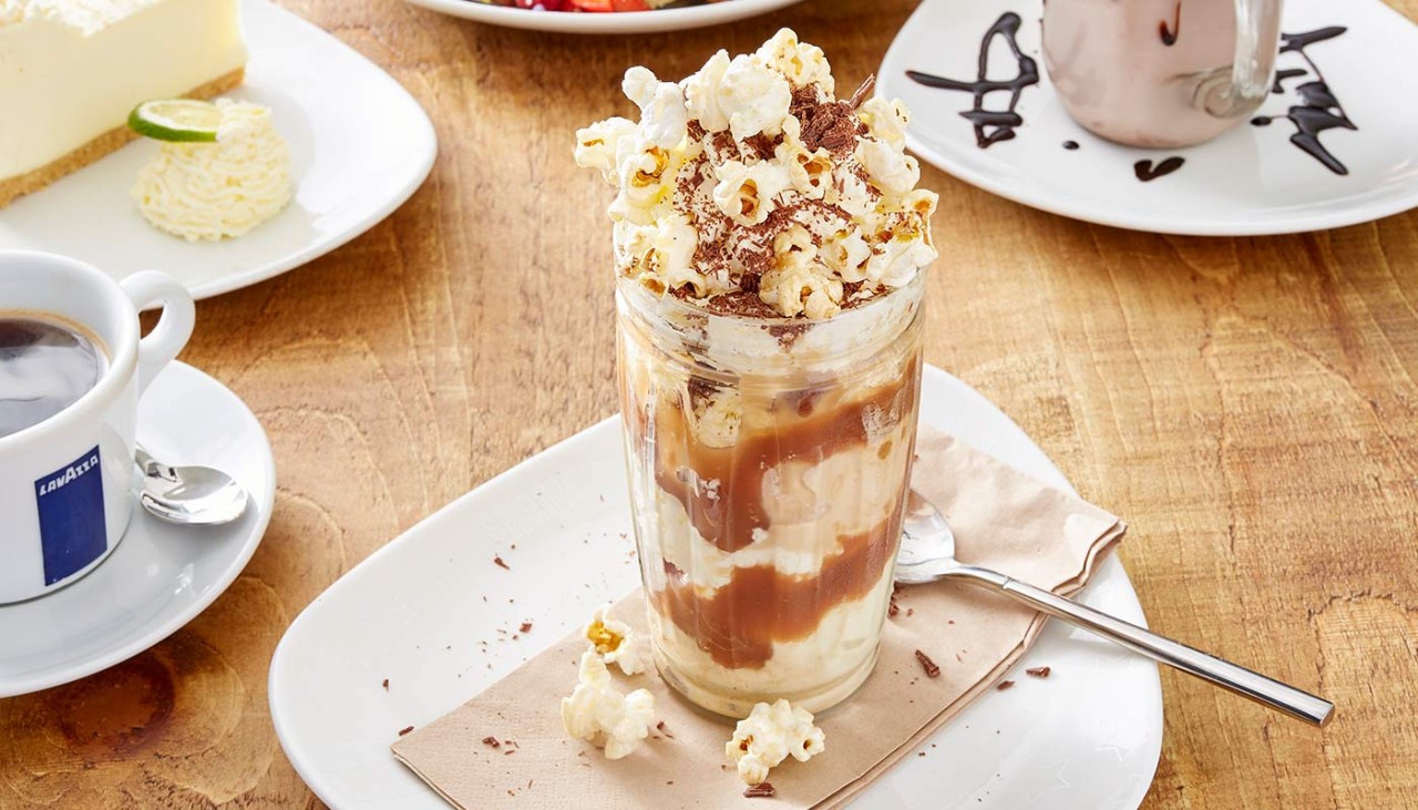 Sundae dessert filled with caramel and cream, topped with popcorn and chocolate sprinkles