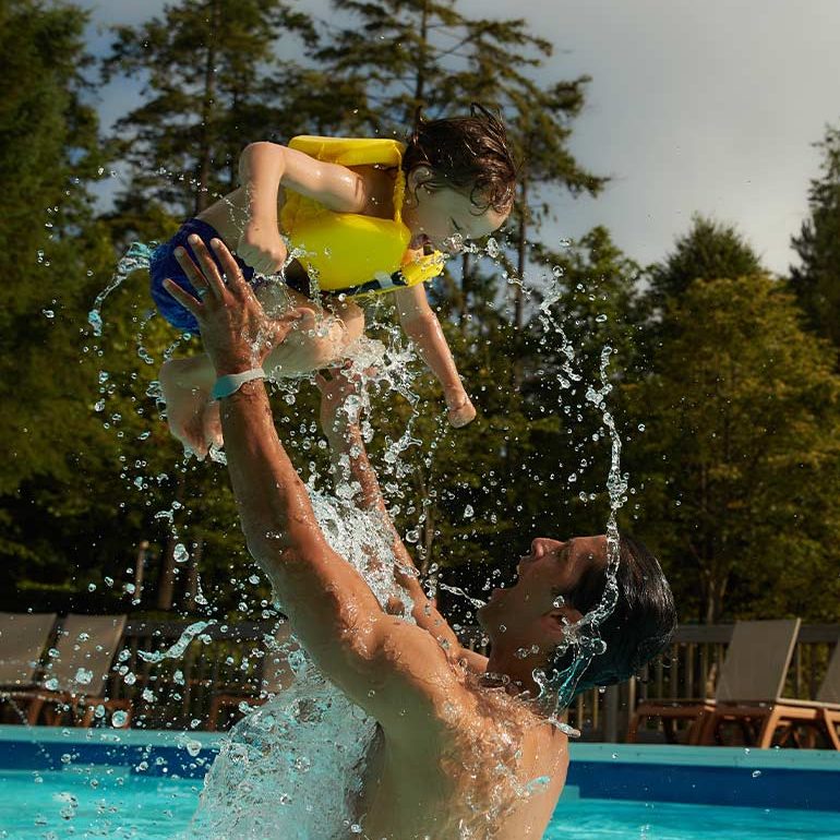 a father lifts his son into the air in the outdoor pool