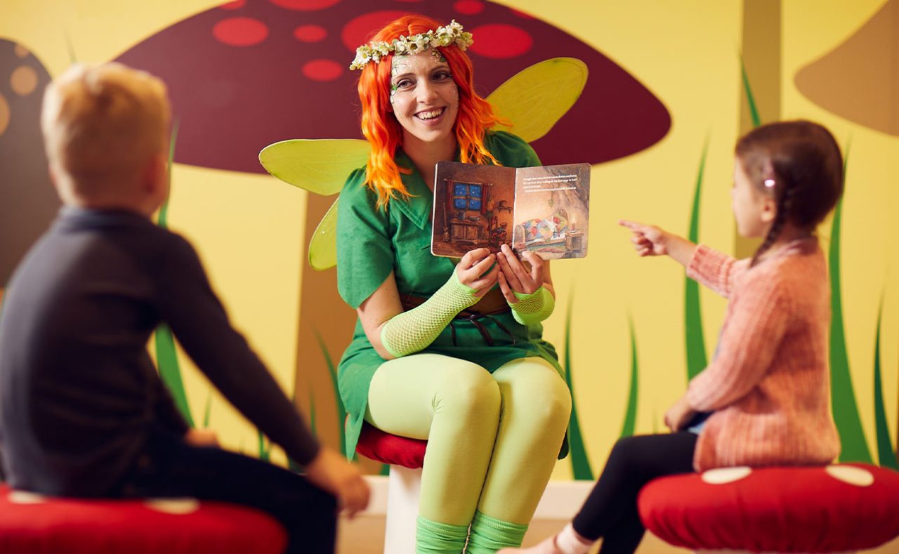 A pixie reading a story to children sat on toadstools