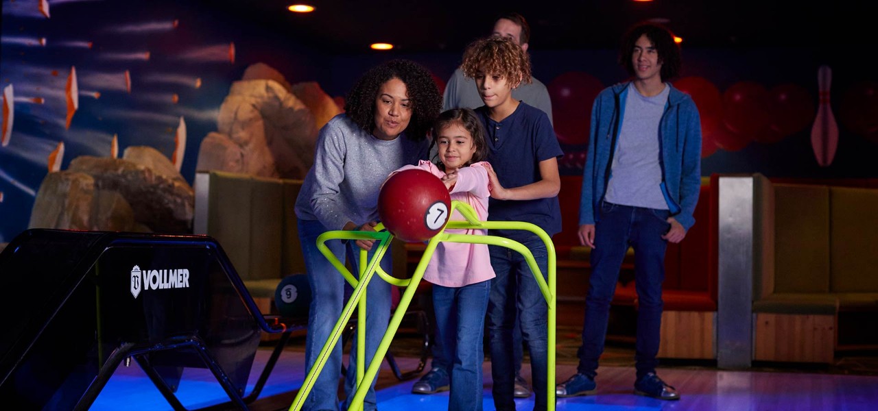 A little girl and her family playing a game of bowling