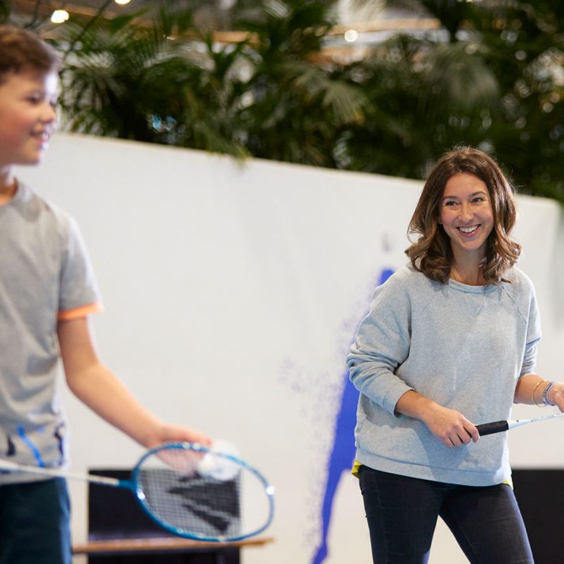 A mother and son smile as they play badminton