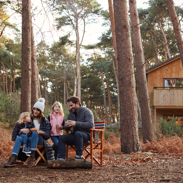 Family sit outside lodge in forest