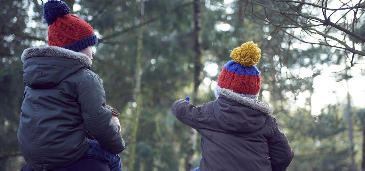 Two children in bobble hats on fathers shoulders in woods