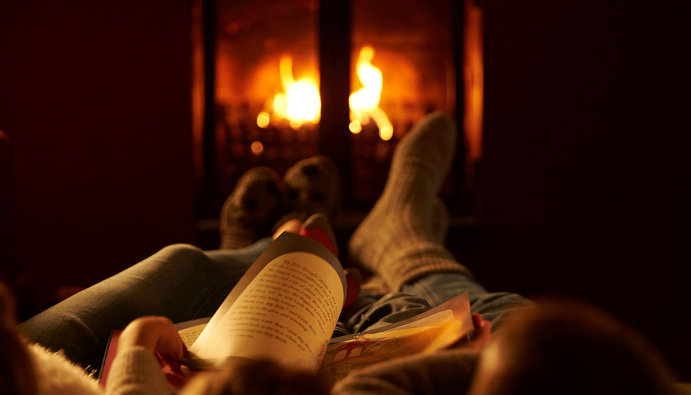 A family snuggled up reading by a fire.