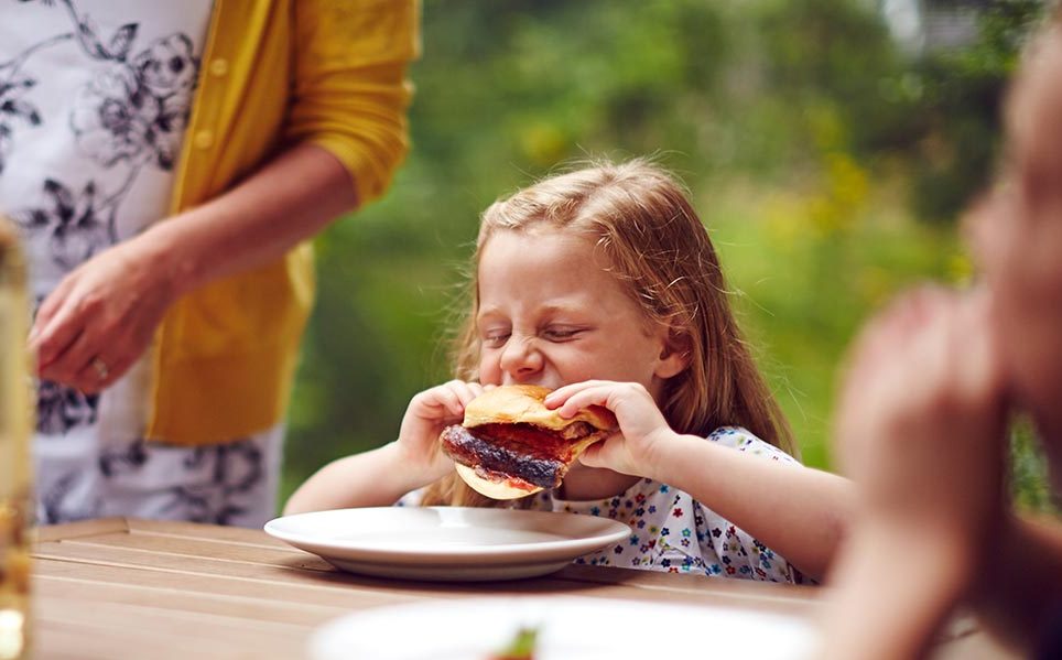 little girl eating a big burger with family 