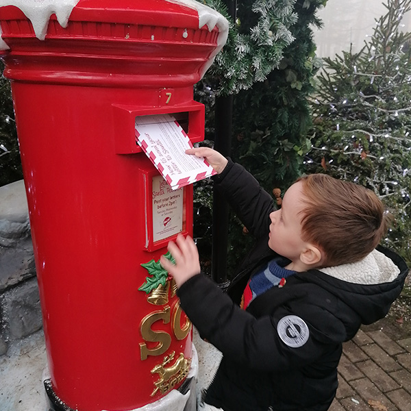 A little boy posting his letter to Santa in a red postbox